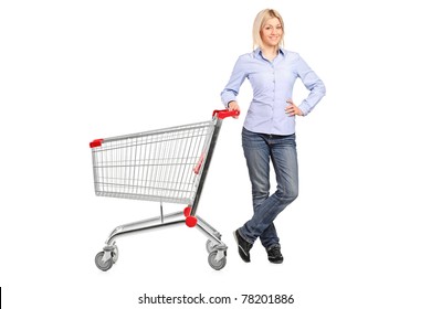 A smiling woman posing next to an empty shopping cart isolated on white background