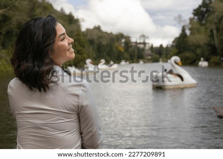 Smiling woman in profile in front of a black lake with swan-shaped pedal boats
