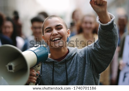 Smiling woman protesting with a bullhorn on the street with people in background. Female with a megaphone as she participates in a street demonstration.