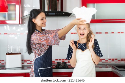 Smiling woman putting a chef hat on her younger friend's head - Powered by Shutterstock