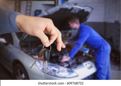 Smiling woman receiving keys from somebody against mechanic examining car engine - Powered by Shutterstock