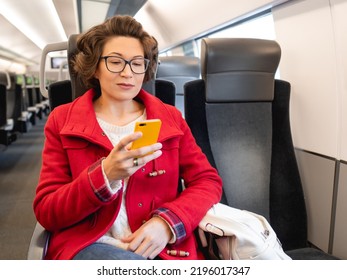 Smiling Woman In Red Duffle Coat Texting On Smartphone In Suburban Train. Travel By Land Vehicle.