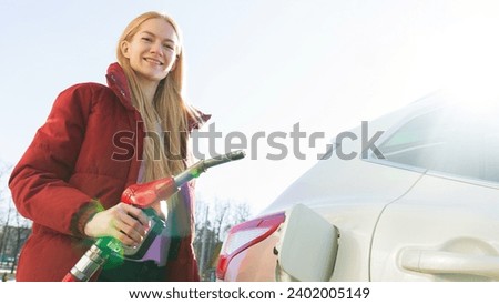 A smiling woman refuels her car at a gas station.