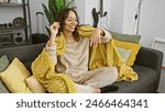 Smiling woman relaxing on a couch with a yellow blanket at home, exuding cozy warmth and positivity.