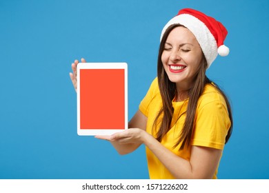 Smiling woman Santa girl in yellow t-shirt Christmas hat posing isolated on blue background. New Year 2020 celebration holiday concept. Mock up copy space. Hold tablet pc computer with blank screen - Powered by Shutterstock