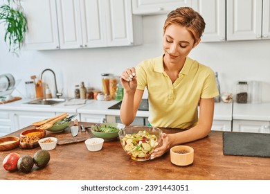 smiling woman seasoning fresh fruit salad with sesame seeds in kitchen, delicious vegetarian diet - Powered by Shutterstock