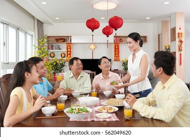 Smiling woman serving family dinner for Tet celebration; couplets with best wishes for coming year in the background