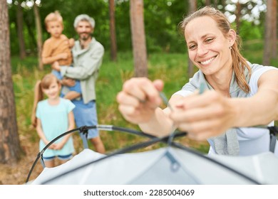 Smiling woman setting up tent while camping with family in summer vacation - Powered by Shutterstock