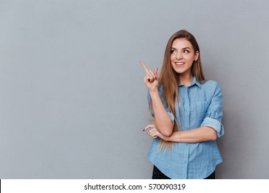 Smiling Woman in shirt posing in studio and pointing up. Isolated gray background
