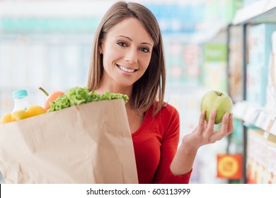 Smiling woman shopping at the supermarket and holding a grocery bag with fresh vegetables, healthy food and lifestyle concept
