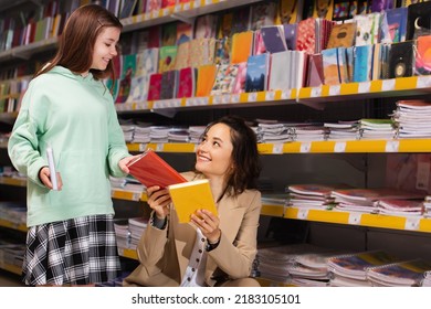 smiling woman showing new colorful copybooks to daughter in stationery store - Shutterstock ID 2183105101