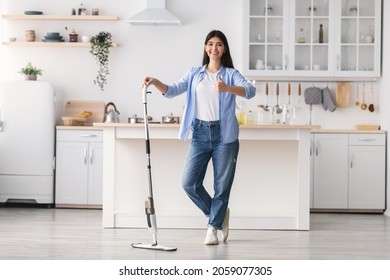 Smiling Woman Showing Thumb Up Sign Gesture After Washing Hardwood Laminate Flooring, Holding And Leaning On Water Spray Mop Pad, Standing At Kitchen Posing At Camera, Full Body Length