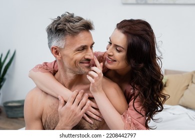 Smiling Woman In Silk Robe Touching Nose Of Shirtless Husband In Bedroom