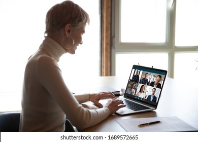 Smiling woman sit at desk have Webcam conference with diverse colleagues at home, businesswoman speak talk on video call with coworkers on online briefing or consultation using Webcam on laptop