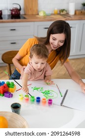 Smiling woman sitting near son drawing at home