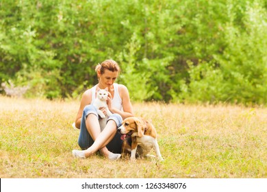 Smiling Woman Sitting On A Grass With Cat And Dog