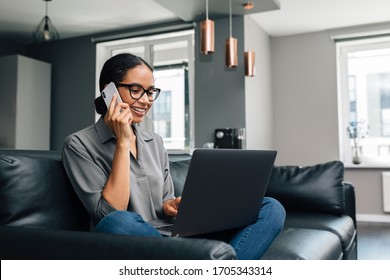 Smiling Woman Sitting On A Sofa With Laptop On Her Legs And Making A Phone Call