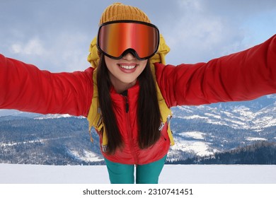 Smiling woman in ski goggles taking selfie in snowy mountains - Shutterstock ID 2310741451