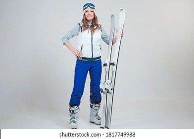 Smiling woman skier in a hat and mask for skiing. A young woman in clothes for skiing and outdoor activities. A woman holds skis and poses on a white background in the Studio.