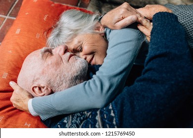 Smiling Woman Sleeping In The Arms Of Her Husband Holding His Head. Happy Senior Couple Sleeping On Floor Hugging Each Other On A Cold Night.