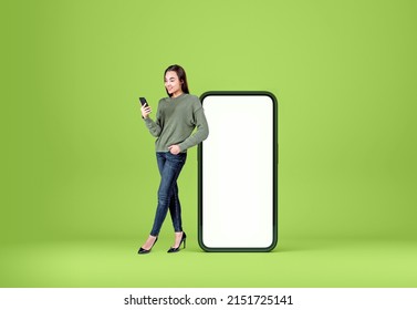 Smiling woman with smartphone, full length near device mock up copy space screen, green background. Concept of mobile app and social media - Shutterstock ID 2151725141
