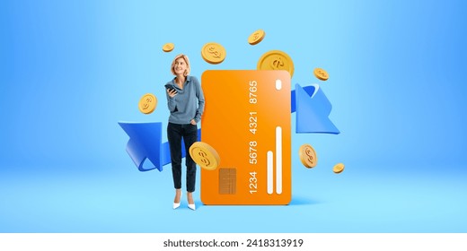 Smiling woman with smartphone, standing near big mock up credit card, falling coins and arrow on blue background. Concept of online payment, mobile banking and cashback