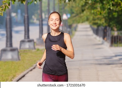 Smiling woman in sportswear goes jogging down street at sunny morning in city