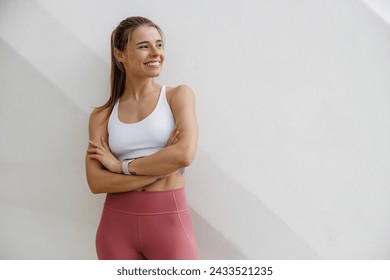 Smiling woman in sportswear have a rest after workout outside standing on building background - Powered by Shutterstock