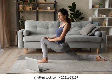 Smiling woman in sportswear practicing yoga online, stretching, looking at laptop screen, watching webinar or involved in internet lesson with coach, attractive young female doing morning gymnastics