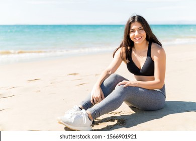 Smiling woman in sportswear relaxing on sea shore after workout at beach 