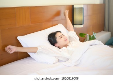A smiling woman stretching her hands after waking up in the morning at home. - Shutterstock ID 1810819009