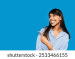 Smiling woman in a striped shirt points playfully against a vibrant blue background, radiating joy and positivity