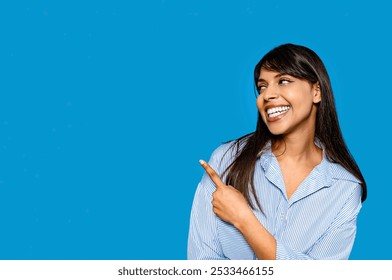 Smiling woman in a striped shirt points playfully against a vibrant blue background, radiating joy and positivity - Powered by Shutterstock