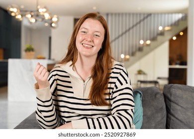 Smiling woman in striped sweater sitting on couch in modern living room, on video call. Interior, casual, lifestyle, relaxation, domestic, comfortable,  - Powered by Shutterstock