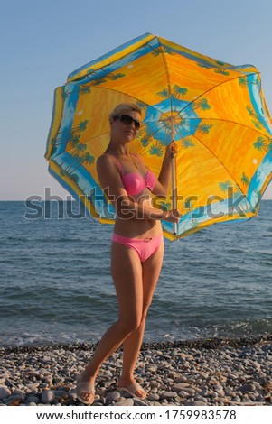 Smiling woman in sunglasses bikini at the seaside under an umbrella in the summer