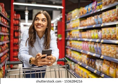 Smiling woman at supermarket. Happy woman at supermarket. Beautiful young woman shopping in a grocery store/supermarket. Shopaholic woman enjoying shopping spree in supermarket