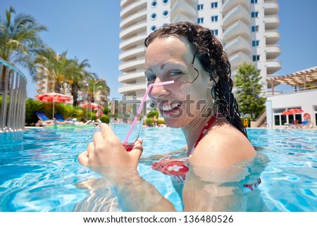 Smiling woman swims in pool with glass of cocktail