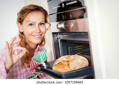 Smiling Woman Takes Out Fragrant And Crunchy Bread From The Oven In The Kitchen