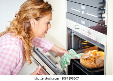 Smiling Woman Takes Out Fragrant And Crunchy Bread From The Oven In The Kitchen