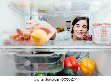 Smiling woman taking a fresh lemon out of the fridge, healthy food concept - Shutterstock ID 603106244
