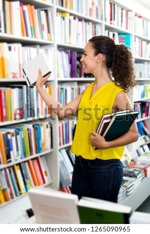 Smiling woman taking literature books in store with prints
