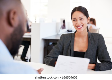 Smiling woman talking to a man at a meeting in a busy office