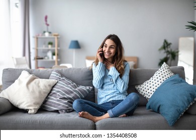 Lächelnde Frau, die zu Hause auf dem Sofa telefoniert. Feminine Klatsch auf dem Smartphone.