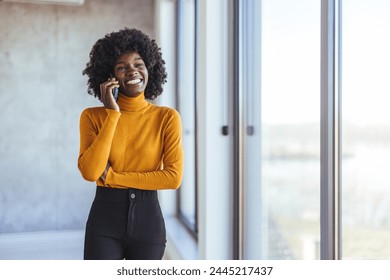 Smiling woman talking on the phone. Handling her business one call at a time. Smiling biracial female hold cell at ear talk look at pc screen. Busy young black lady advisor lawyer give phone consultat - Powered by Shutterstock