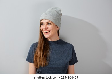 Smiling woman in teenage style and beanie hat standing near wall and looking at side.