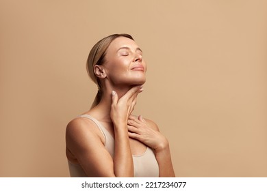 Smiling Woman Touching Neck. Waist up Portrait of Attractive Woman Touching her Skin and Smiling with Closed Eyes. Woman Appearance and skin Care Concept 