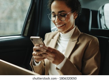 Smiling woman traveling by a car. Businesswoman sitting on backseat of a car and reading text message. - Powered by Shutterstock