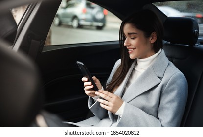 Smiling woman traveling by a car. Businesswoman sitting on backseat of a car and reading text message. - Powered by Shutterstock