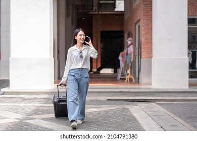 Smiling woman traveller talking using smartphone and dragging black suitcase luggage bag walking to passenger boarding in airport, Travel concept.