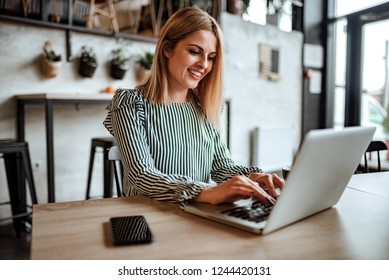 笑顔の女性が室内でノートパソコンをタイプしている。